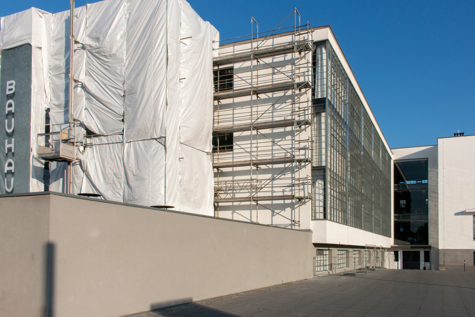 Baugerüst vor der Südseite des Bauhausgebäudes. Auf einem Banner ist der Bauhausschriftzug gedruckt. Es hängt an der Stelle des ursprünglich historischen Schriftzugs.