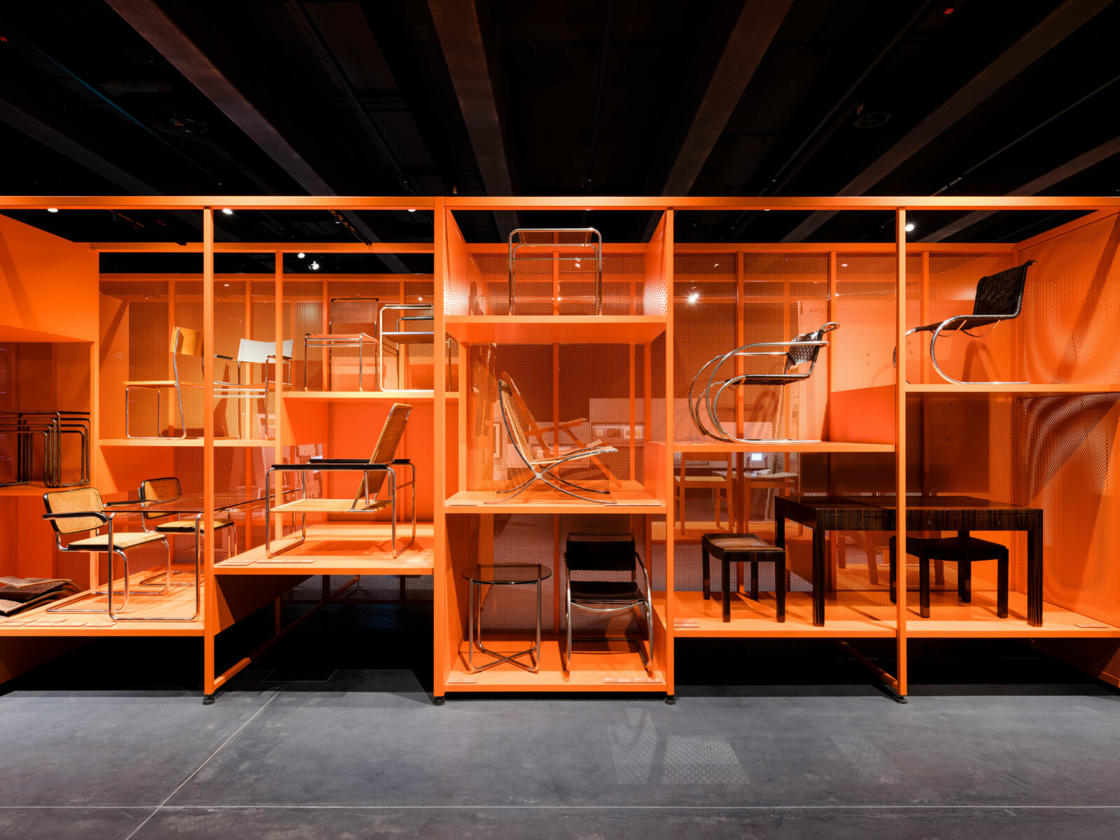 Oragnefarbenes Regal in der Dauerausstellung. Darin stehen bekannte Stühel und Tische, die von Bauhäuslern entworfen wurden.