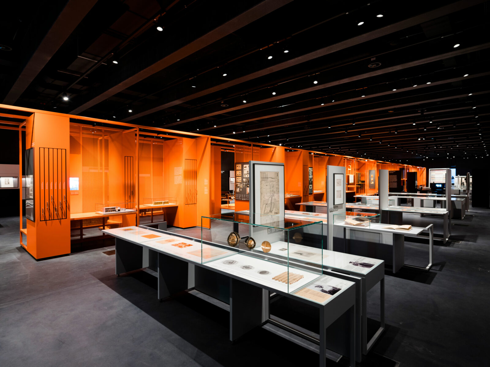 In der Mitte des langgezogenen Ausstellungsraums befindet sich ein orangefarbenes Regal in dem die Produkte des Bauhauses wie in ein Regal eingefügt stehen.