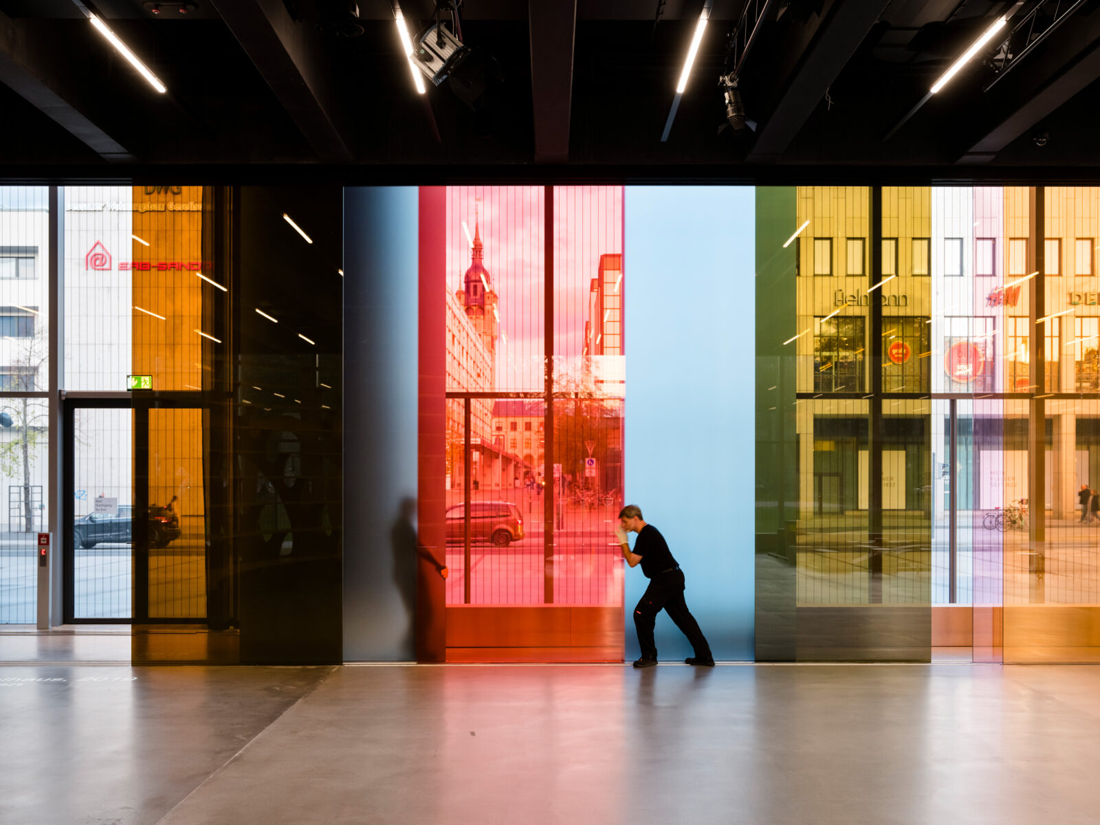 Große bunte, lichtdurchlässige Glassscheiben werden durch Männer verschoben. Das ist die Kunst am Bau im Bauhaus Museum Dessau.