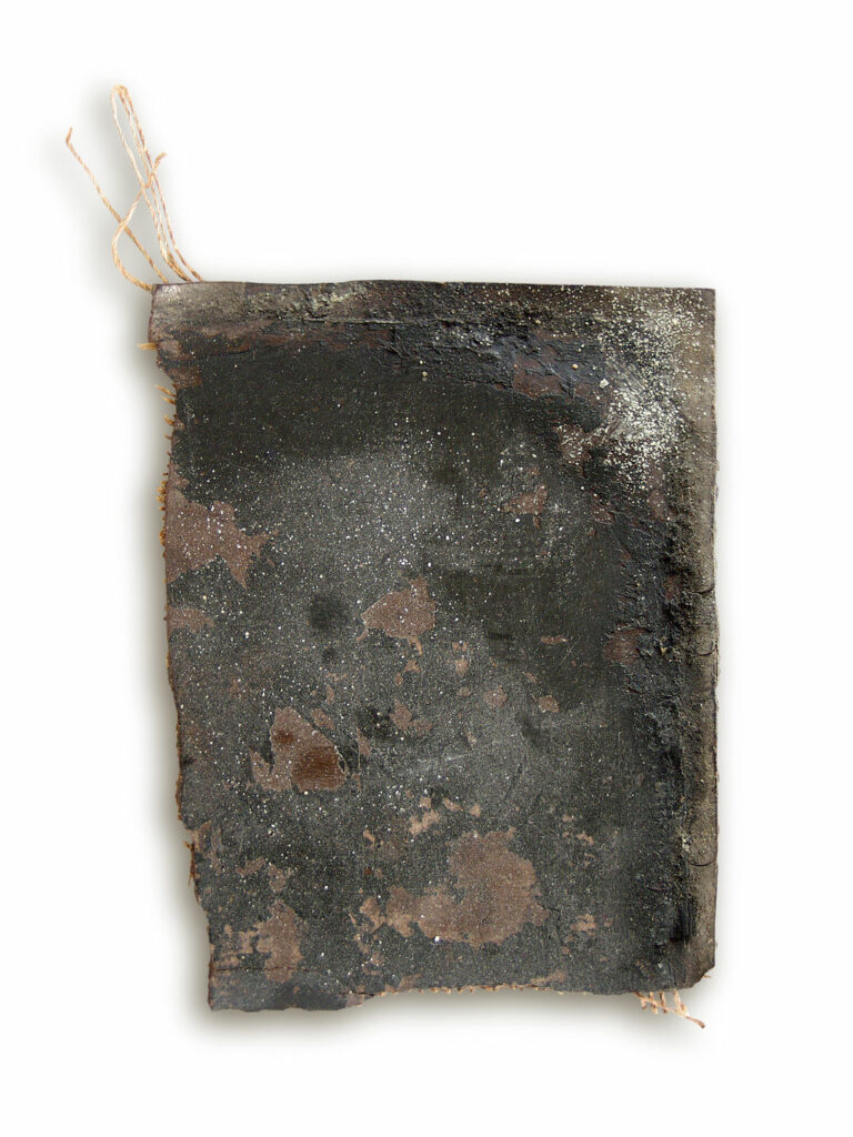 Ein dunkelbraunes, fleckiges altes Stück Triolin-Fußbodenbelag. Am Rand ragen ein paar Gewebebänder heraus.