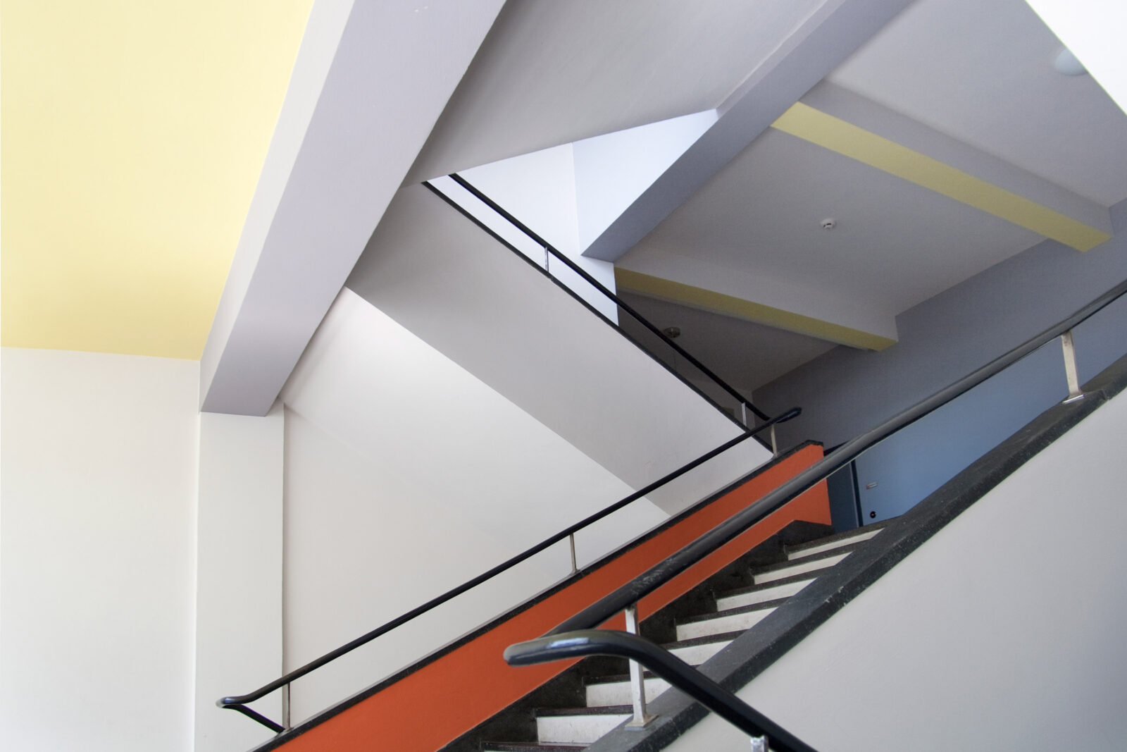 Treppenhaus im Bauhausgebäude. Die Decken und Wände sind in den Farben Gelb, Rot, Graublau und Grau gestrichen.