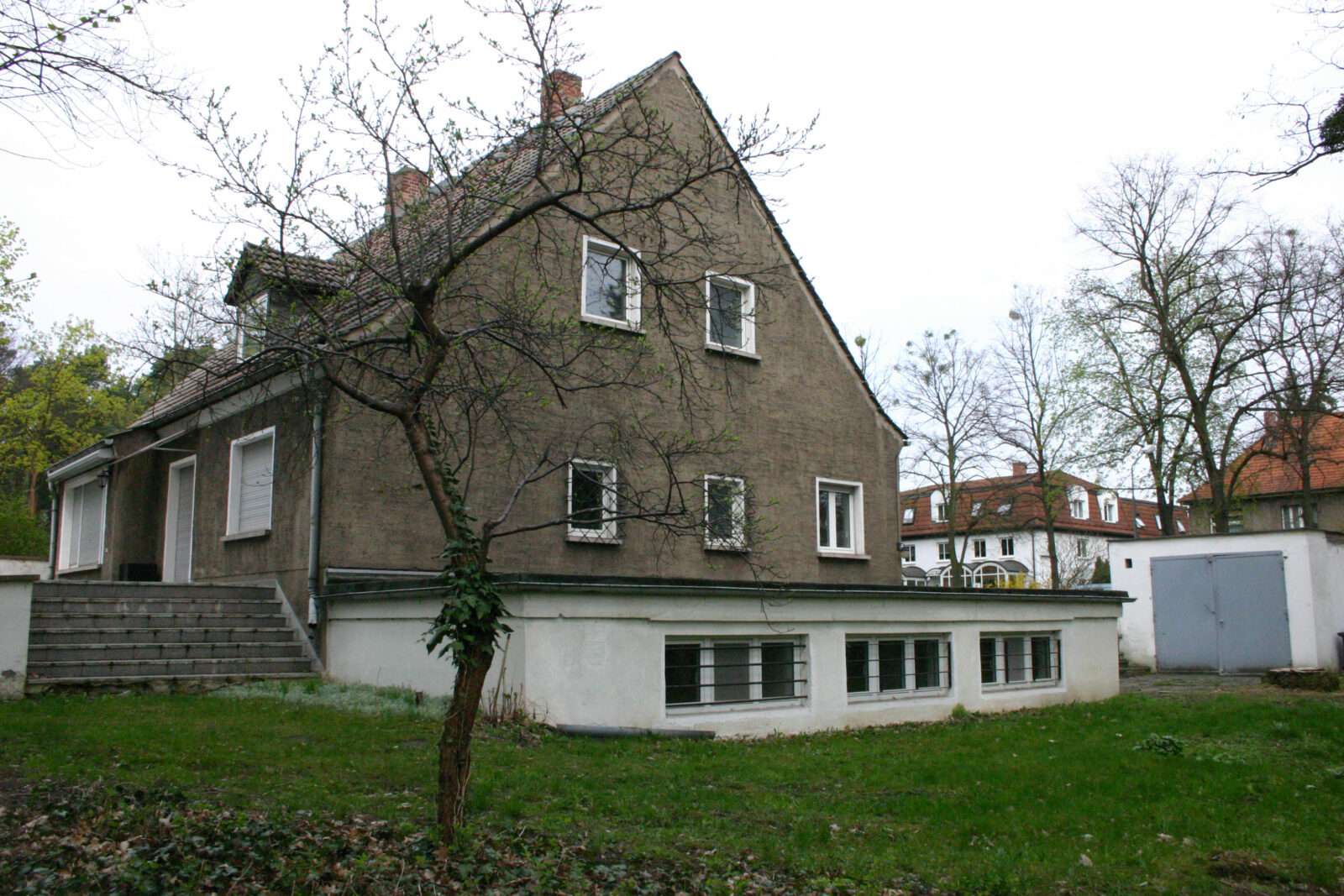 Grau verputztes Einfamilienhaus mit Satteldach. Nur das historische Sockelgeschoss ist weiß gestrichen.