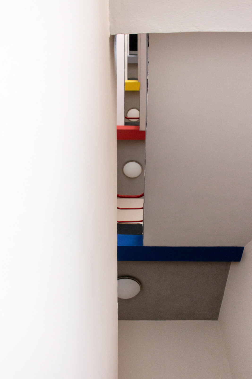 Blick im Treppenhaus des Ateliergebäudes von unten nach oben. Die verscheidenen Etagen grenzen sich durch die Farbenen Blau, Rot und Gelb voneinander ab.