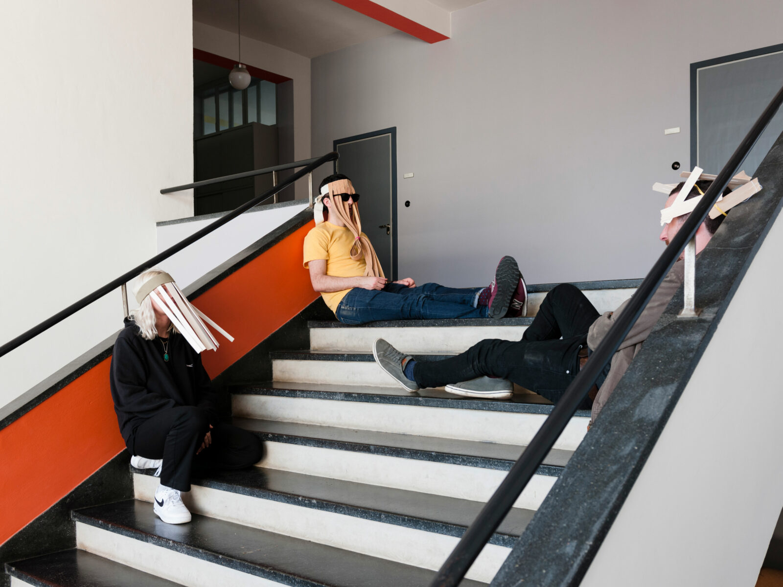 Drei Personen sitzten mit Masken auf der Treppe im Bauhausgebäude.