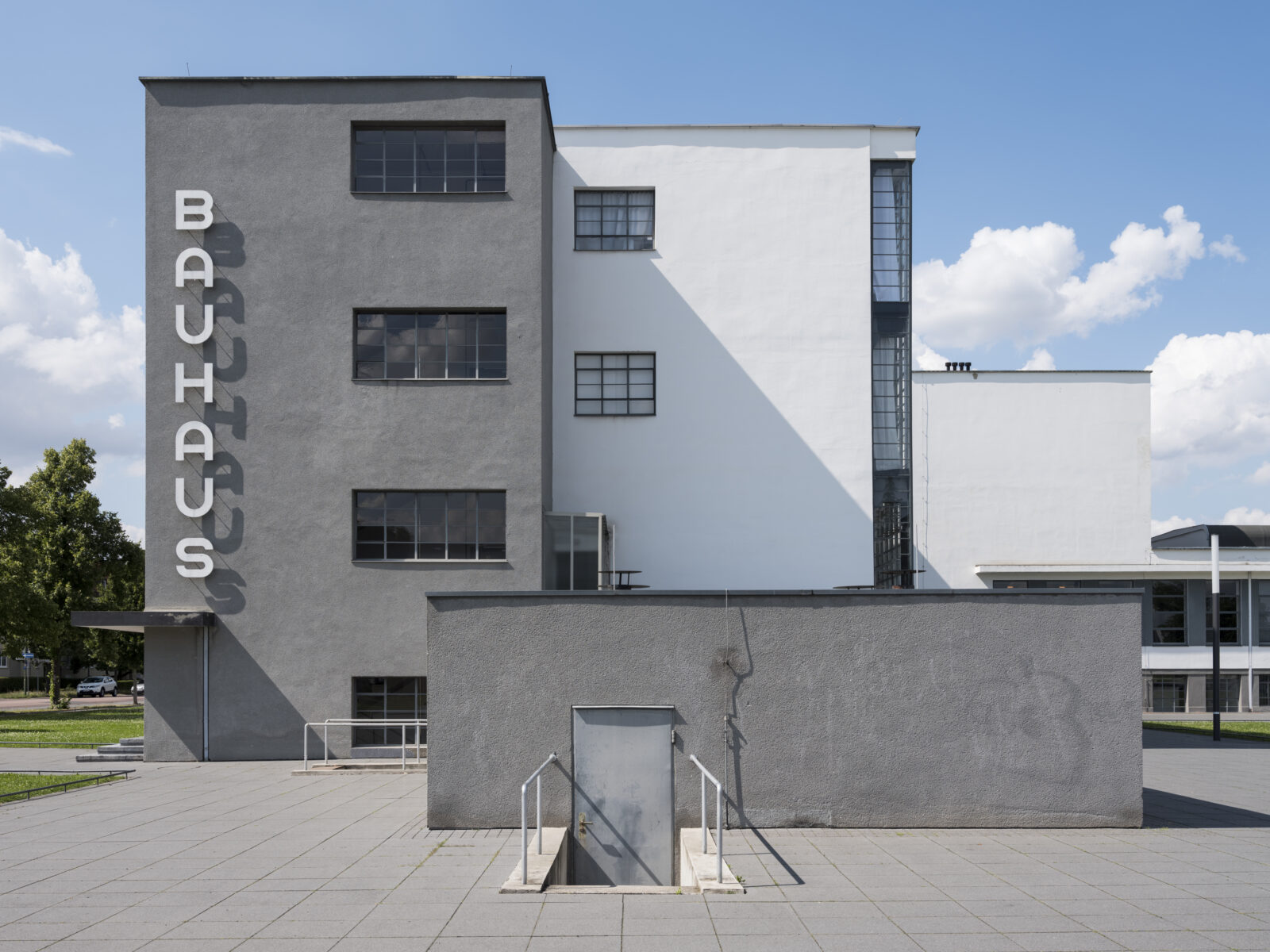 Frontaler Blick auf die Südfassade des historischen Bauhausgebäudes mit dem großen, vertikalen Bauhaus-Schriftzug, bei Sonnenschein und blauem Himmel.